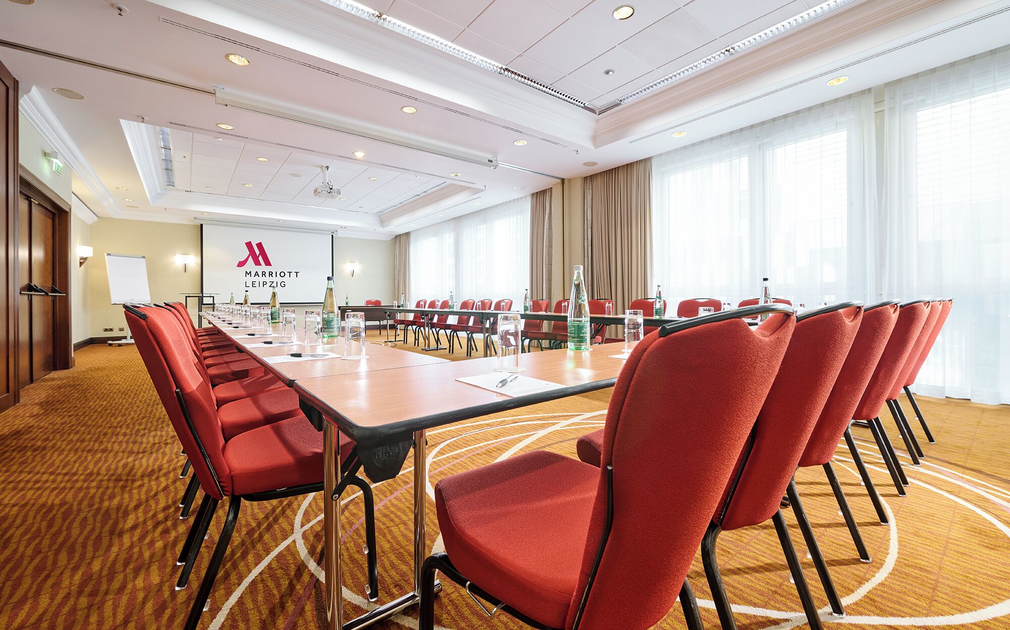 Ein Konferenzraum mit einem langen Tisch, roten Stühlen und dem Marriott-Logo an der Wand.