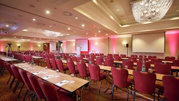 Ein Konferenzraum mit Tischen und Stühlen, einer Projektionsleinwand und einer Kristallleuchtre.