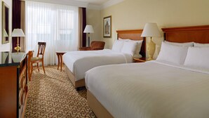 A hotel room with two beds, a desk, a chair, and a large window with curtains. - Leipzig Marriott Hotel (Leipzig)