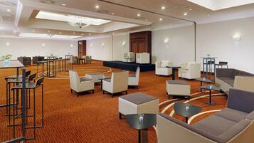 Un amplio vestíbulo de hotel con varias zonas de estar, incluyendo sofás y sillones, distribuidos alrededor de mesas y un escenario.