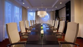 A conference room with a long table, multiple chairs, a chandelier, and a view of the city through large windows.