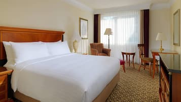 Una habitación de hotel con una cama grande, un escritorio, dos sillas, una lámpara y un espejo.