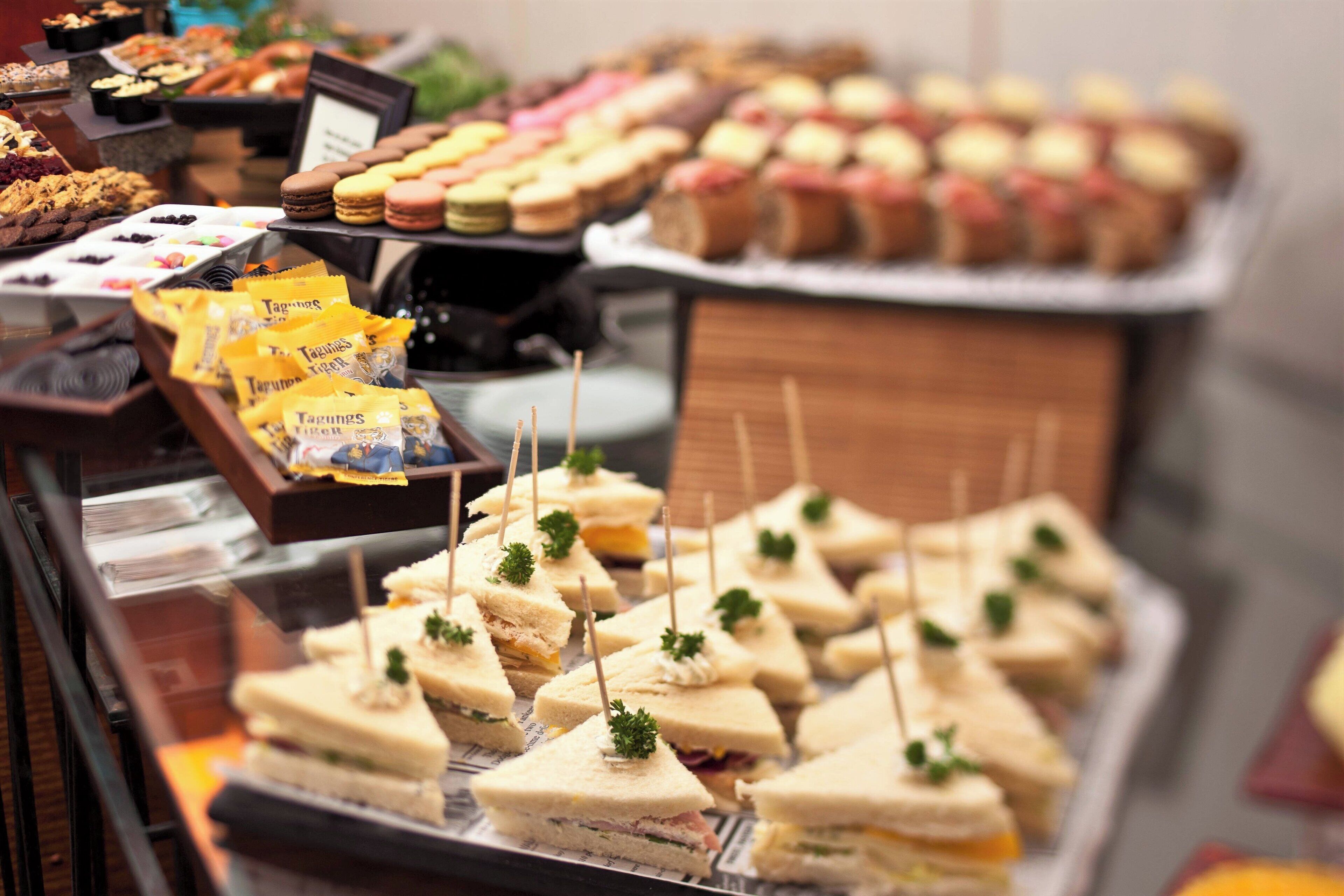 A display of assorted sandwiches and pastries, including macarons and cookies, arranged on trays.