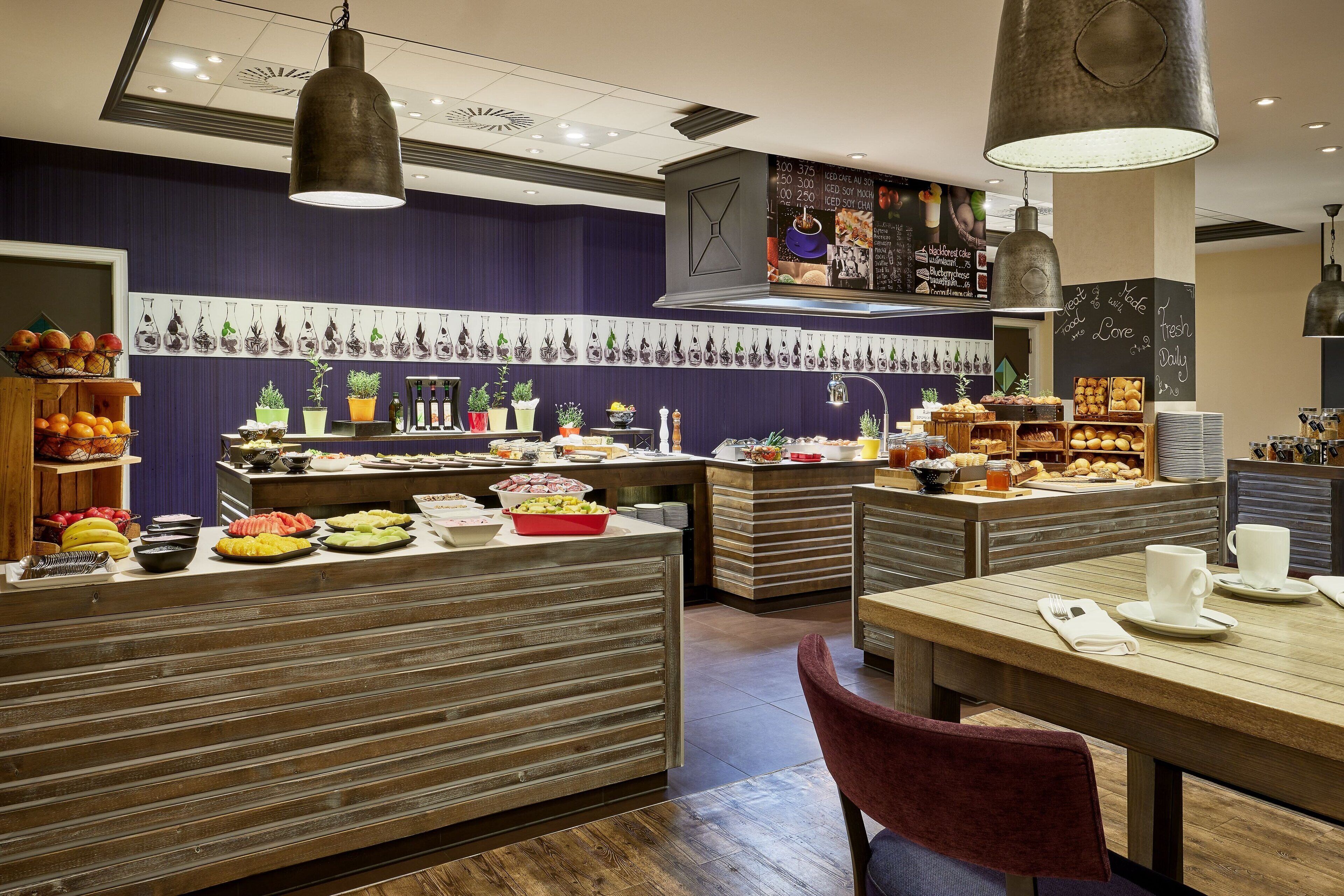 Ein Restaurantinneres mit Holztischen und -bänken, verschiedenen Speisen, die auf Theken präsentiert werden, und hängenden Pflanzen an der Wand.