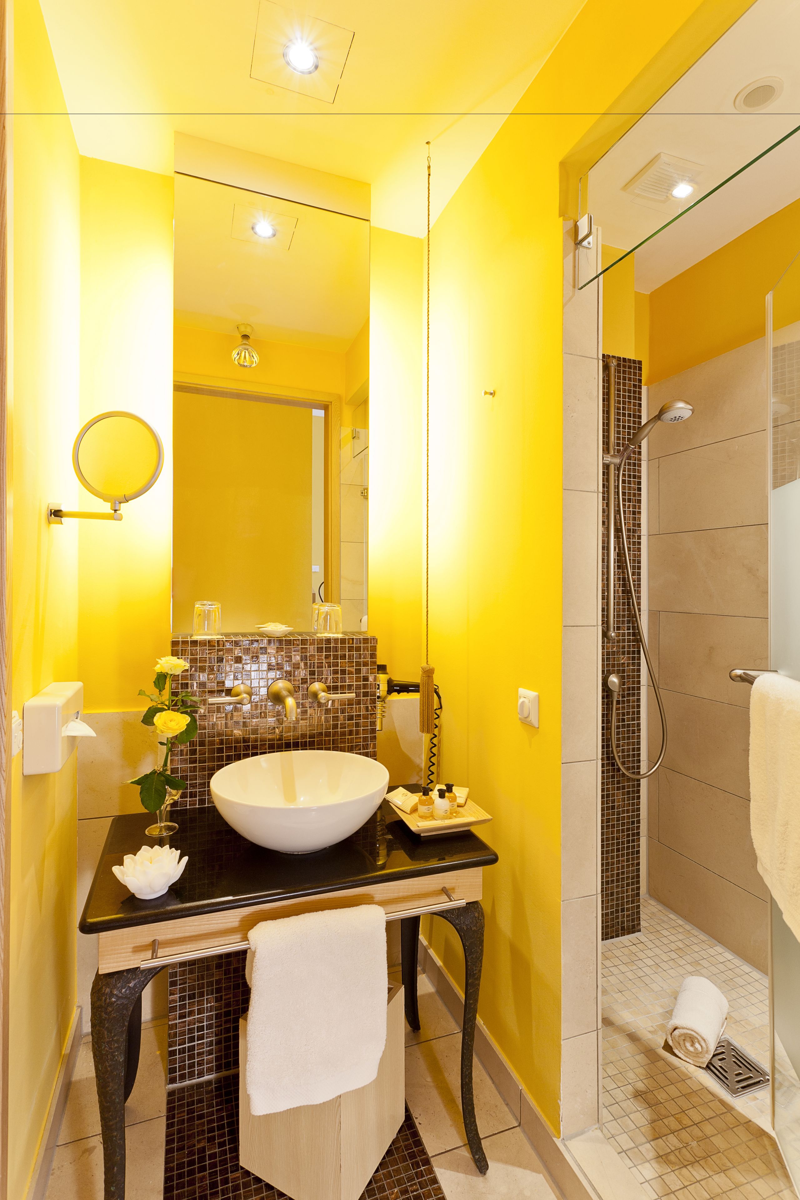 A bathroom with a yellow wall, a white sink, a mirror, and a shower area.