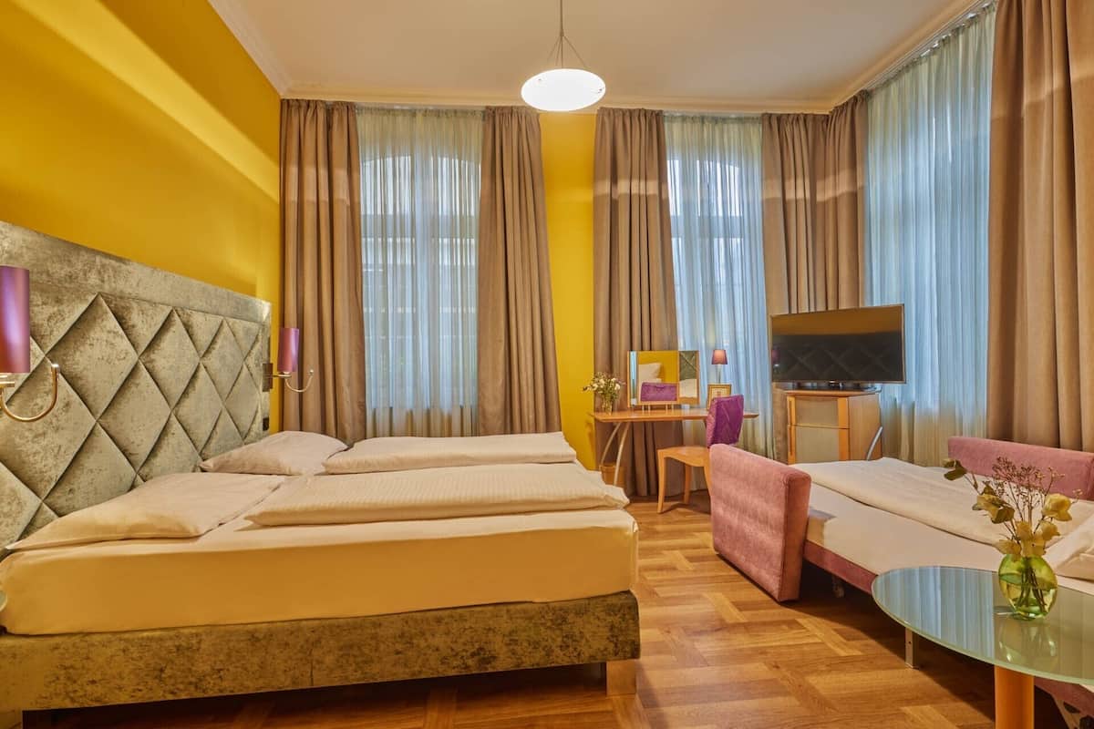 A hotel room with a bed, a sofa, a TV, and a small table with a vase.