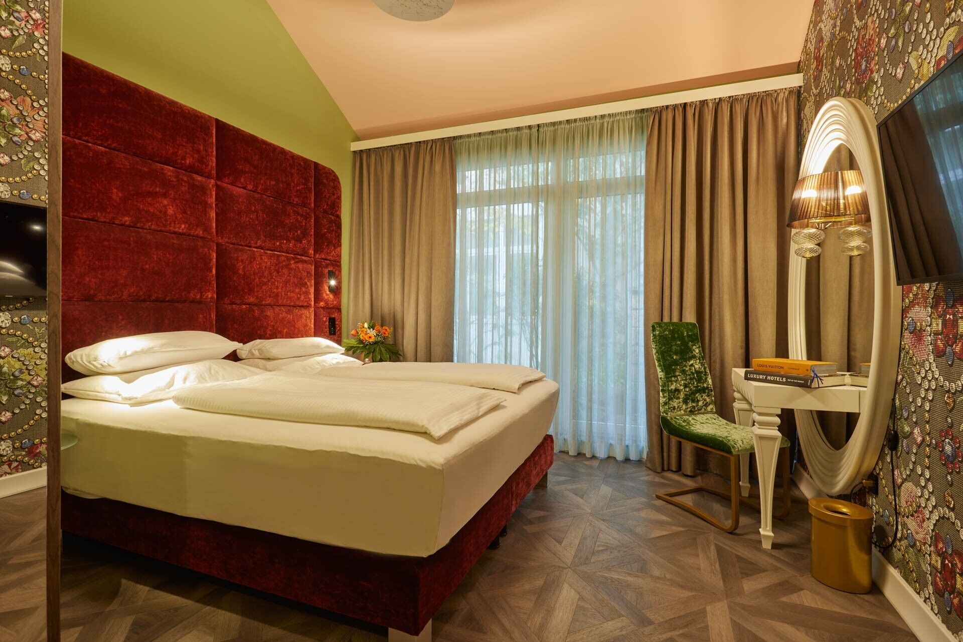 Ein Hotelzimmer mit einem großen Bett, einem Schreibtisch mit Stuhl, einem Spiegel und einem Fernseher.