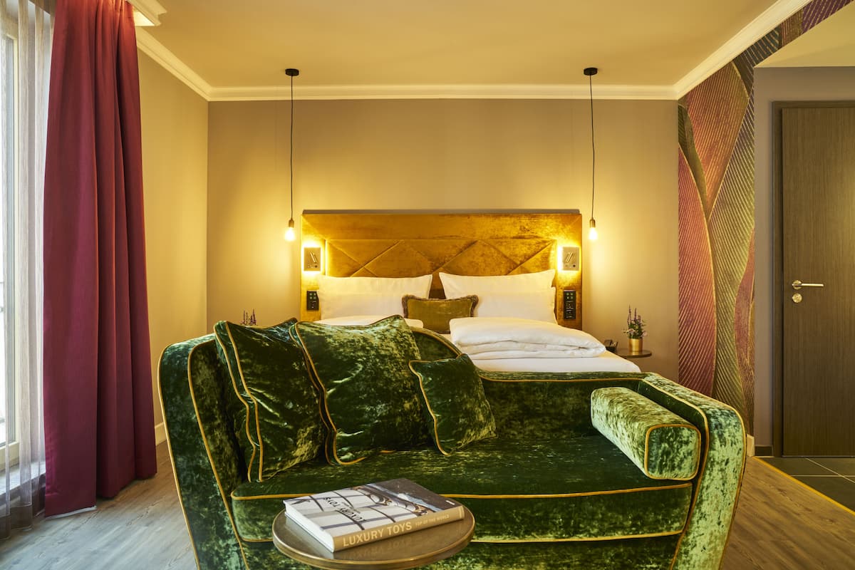 A hotel room with a large bed, a green velvet sofa, and a small table with a book.