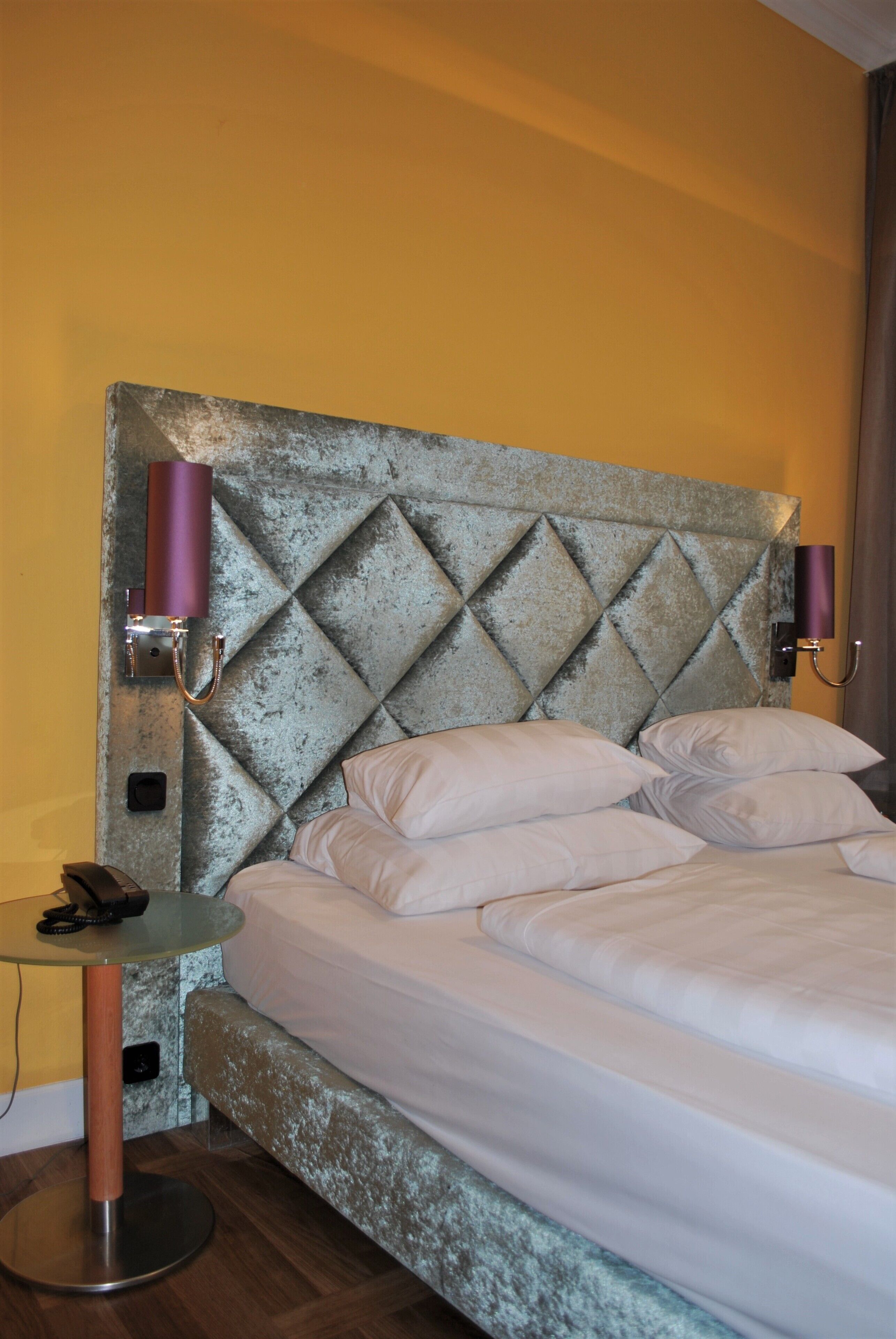A hotel room with a large bed, a small table, and two wall-mounted lamps.