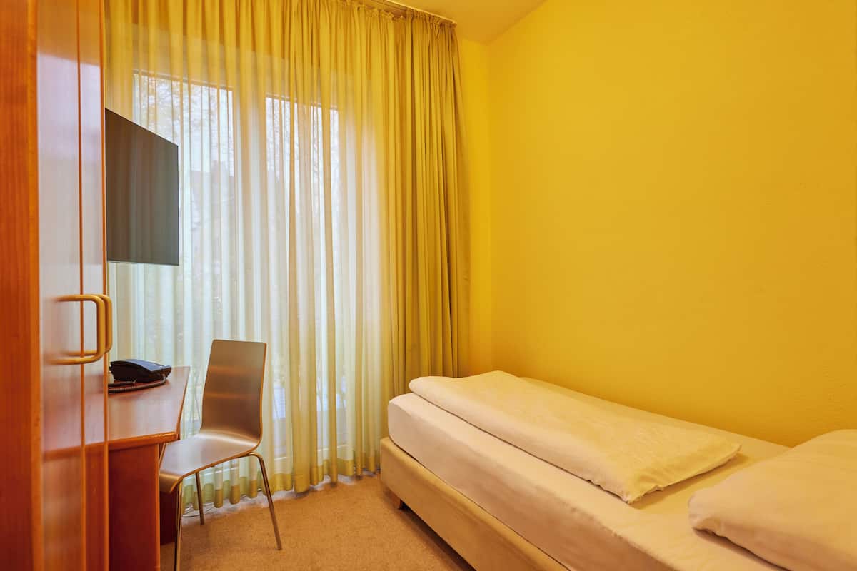 A room with a bed, a desk, a chair, and a window with curtains.