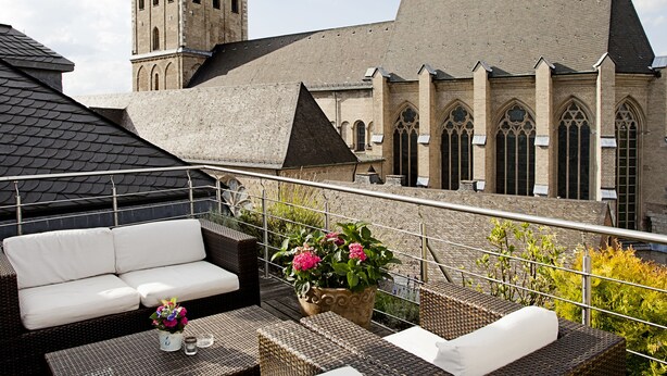Terraza en la azotea con mobiliario de mimbre y vistas a un edificio histórico con una torre.