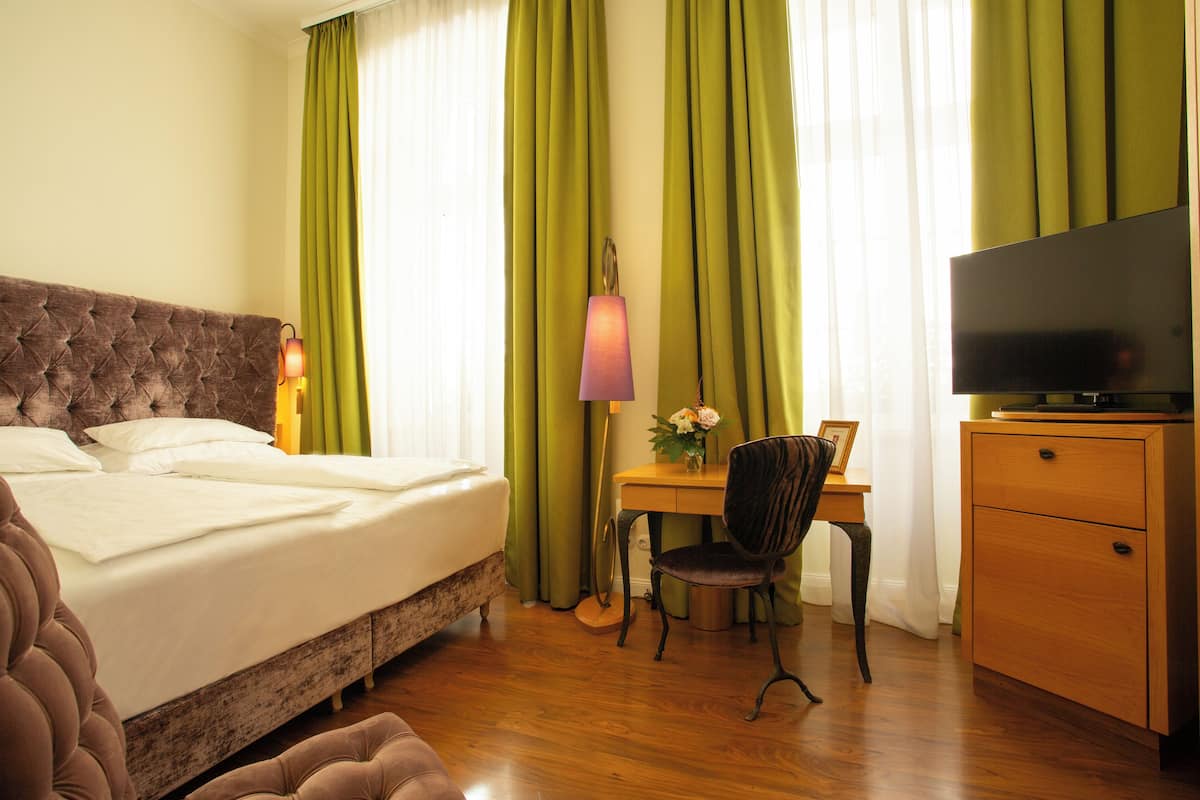 A hotel room with a bed, a desk, a chair, a television, and a wardrobe.