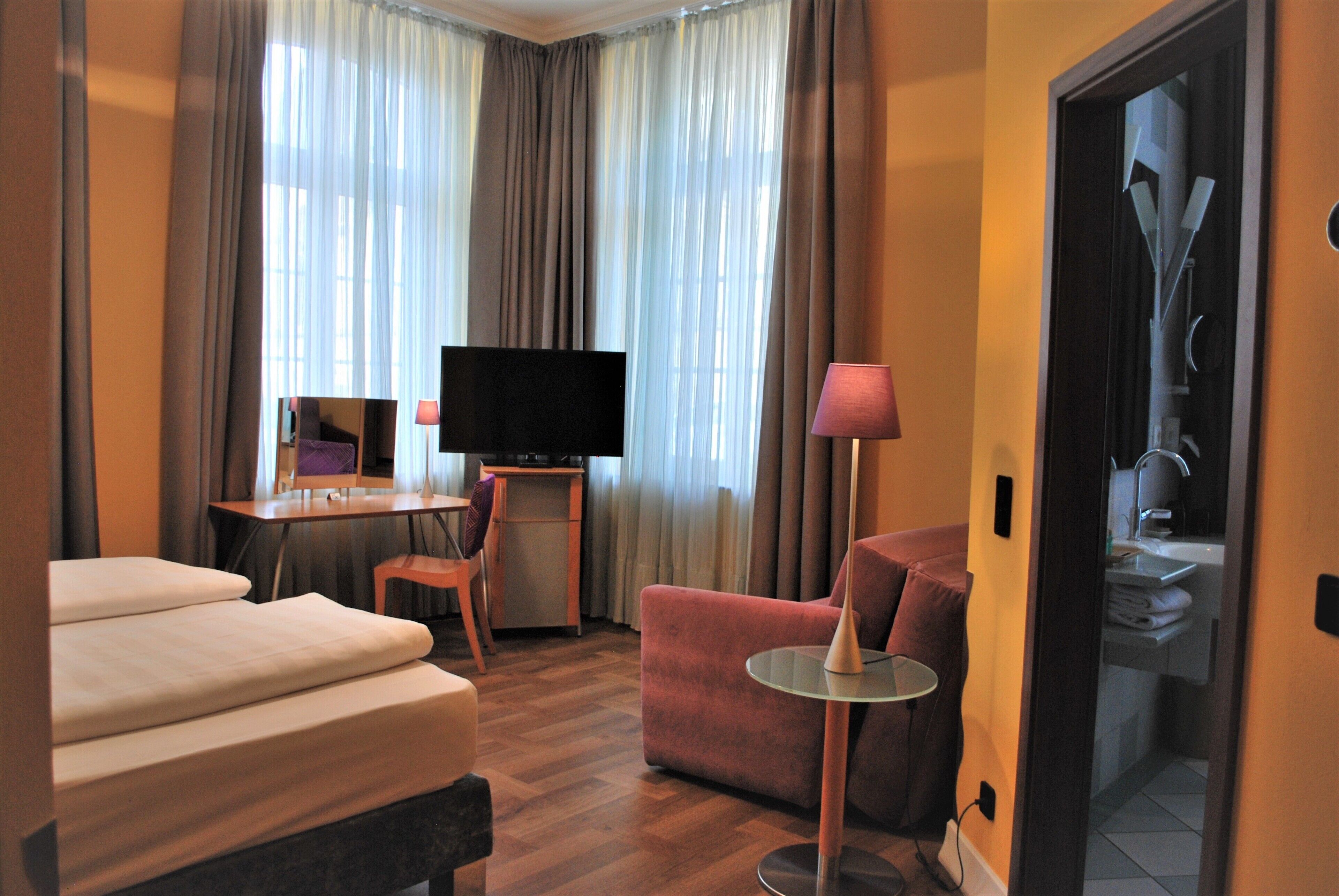 A hotel room with a bed, a desk, a TV, a chair, and a lamp.