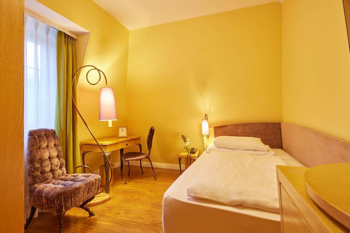 A hotel room with a bed, a desk, a chair, and a lamp.