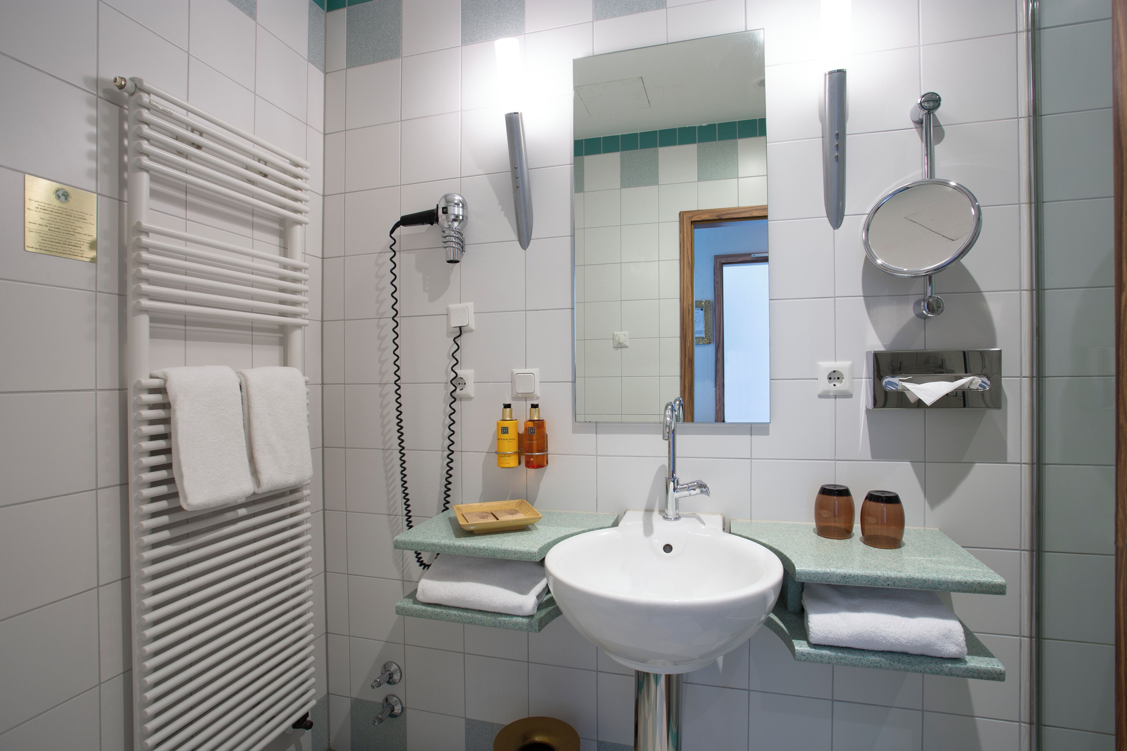 Un baño moderno con un lavamanos blanco, un espejo, un perchero para toallas y una ducha.