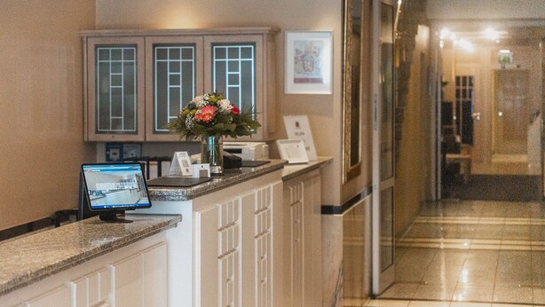 A reception desk with a computer, a vase with flowers, and a framed picture on the wall.