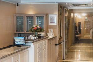 A reception desk with a computer, a vase with flowers, and a framed picture on the wall. - Hotel Daniel (Munich)