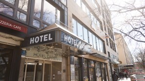 A hotel with a prominent sign, a visible entrance, and a neighboring building with a cafe.