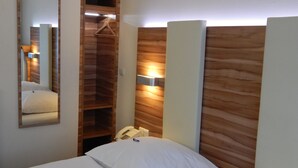 A hotel room with a wooden headboard, a bedside telephone, and a mirror on the wall.