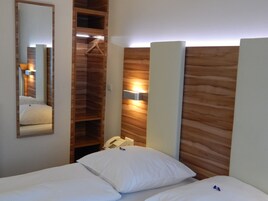Habitación de hotel con cabecera de madera, teléfono en la mesita de noche y espejo en la pared.