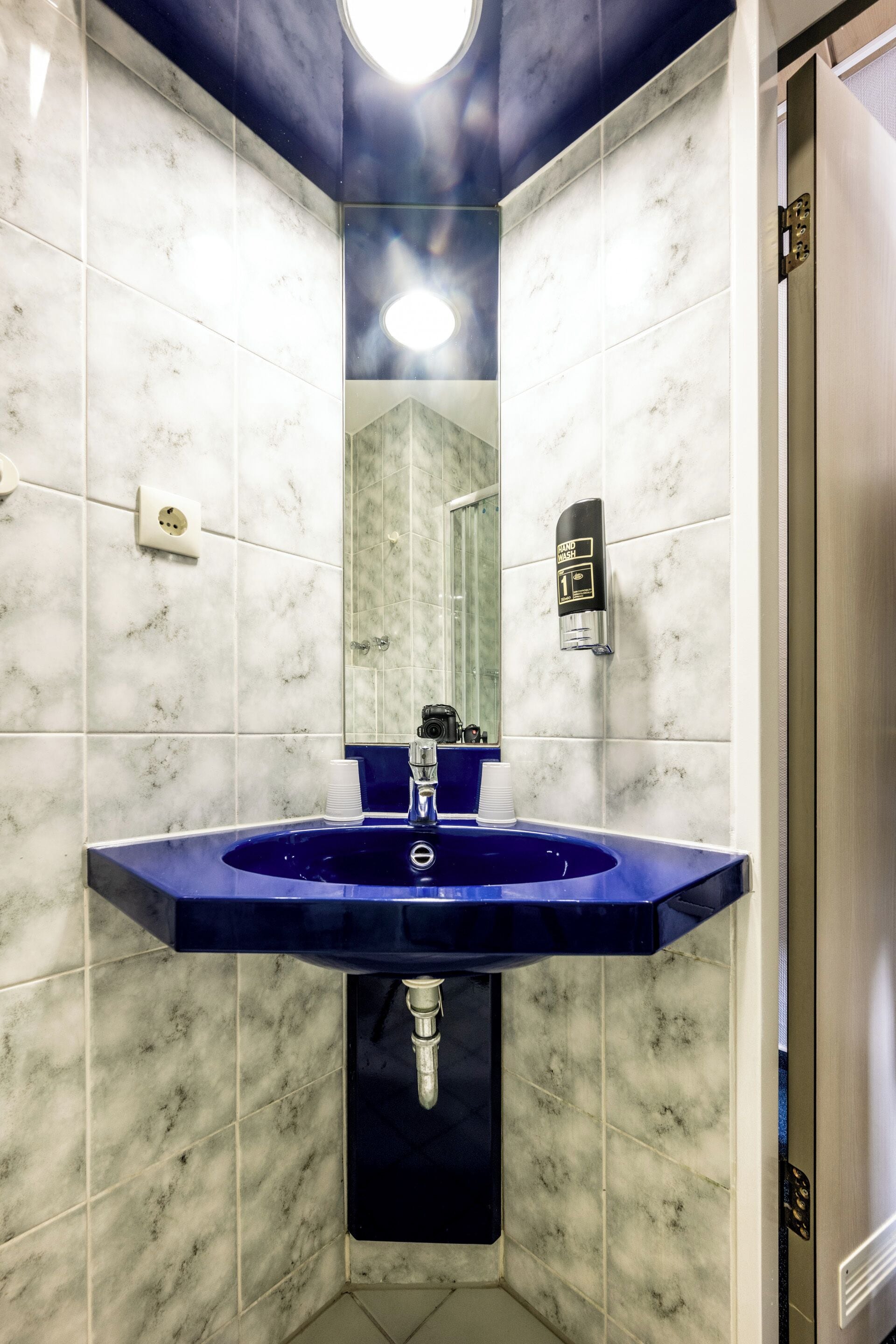 A bathroom with a blue sink, white marble tiles, a mirror, and a light fixture.