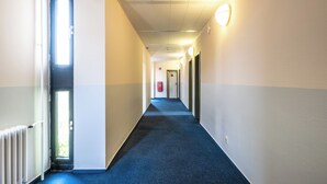 A corridor with a blue carpet, white walls, and a door at the end. - Raststättenhotel Avus (Berlin)