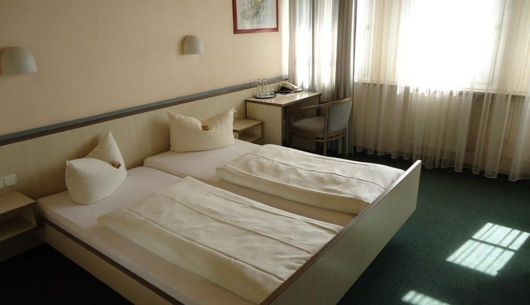 A hotel room with a bed, a desk, a chair, and a window with curtains.