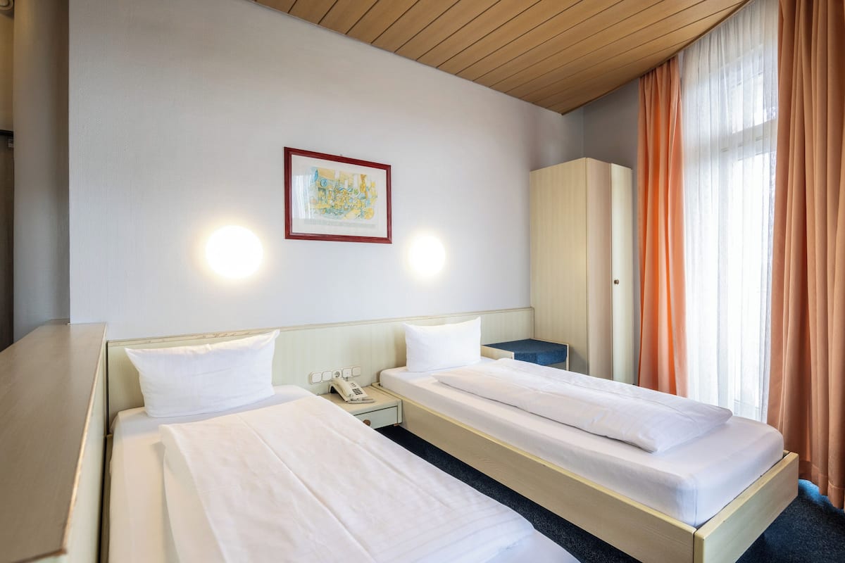 A hotel room with two beds, a nightstand with a phone, a framed picture on the wall, and a wardrobe.