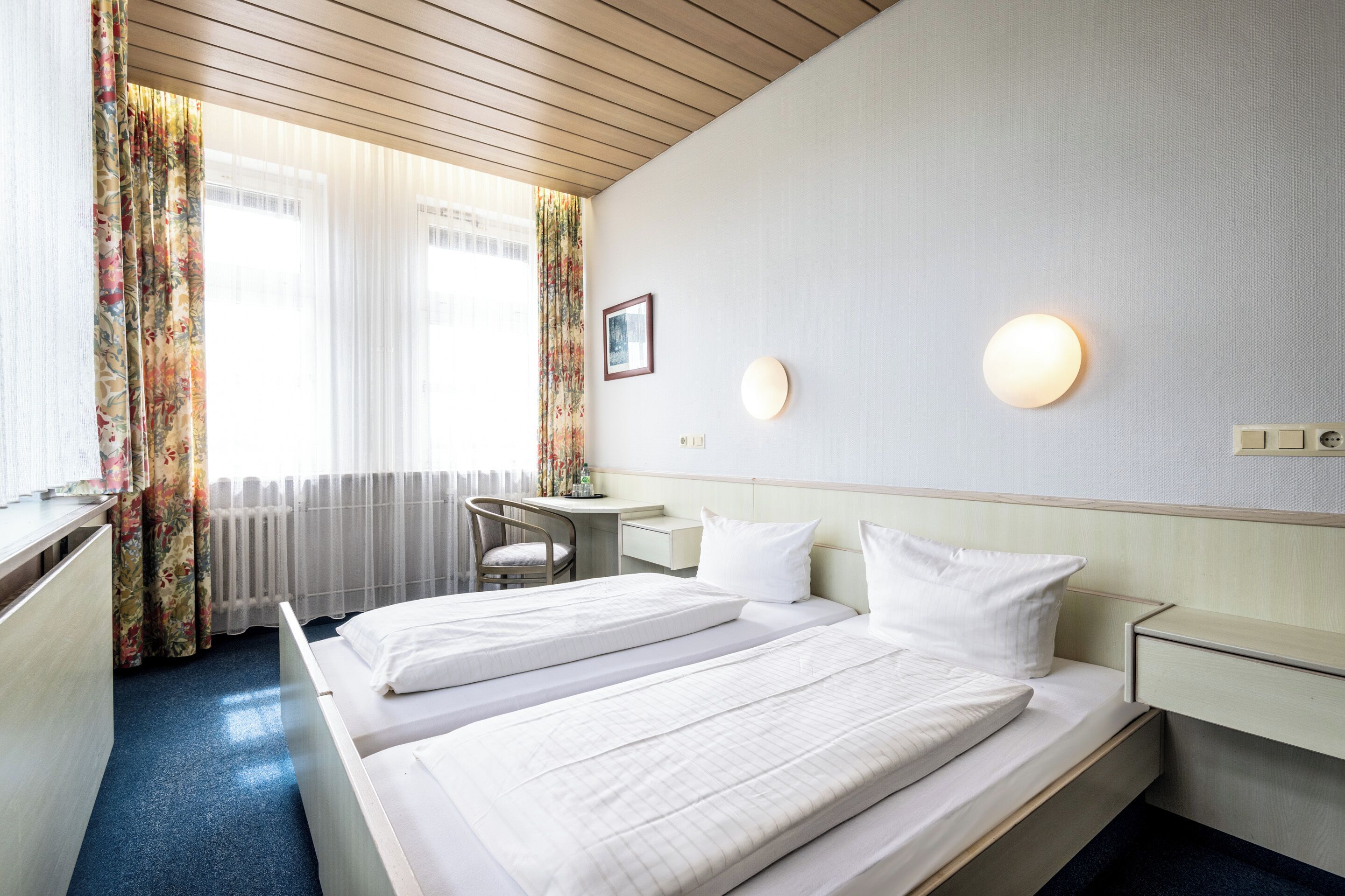 A hotel room with two beds, a desk, and a chair.