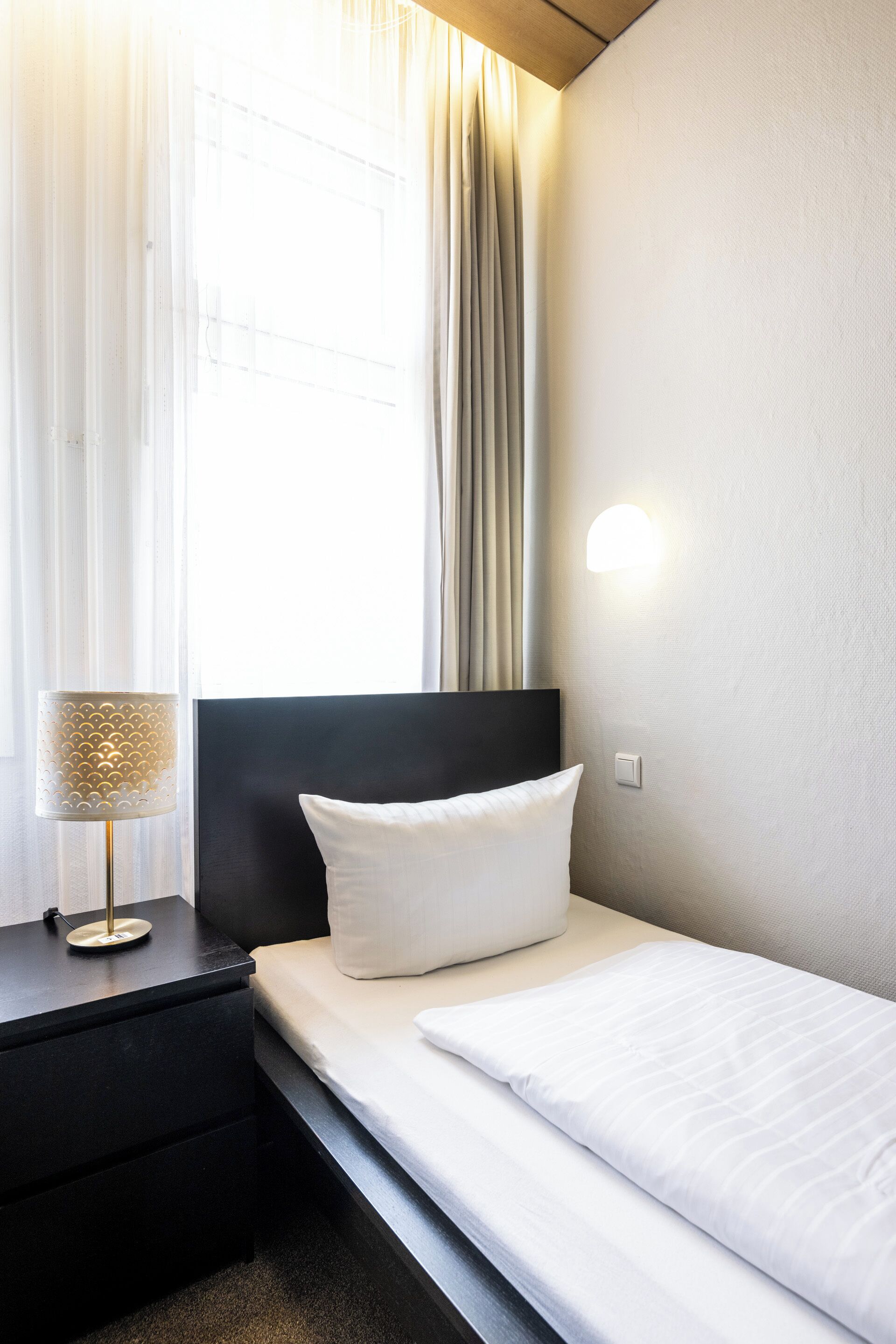 A neatly made bed with a white pillow and a black headboard in a hotel room.