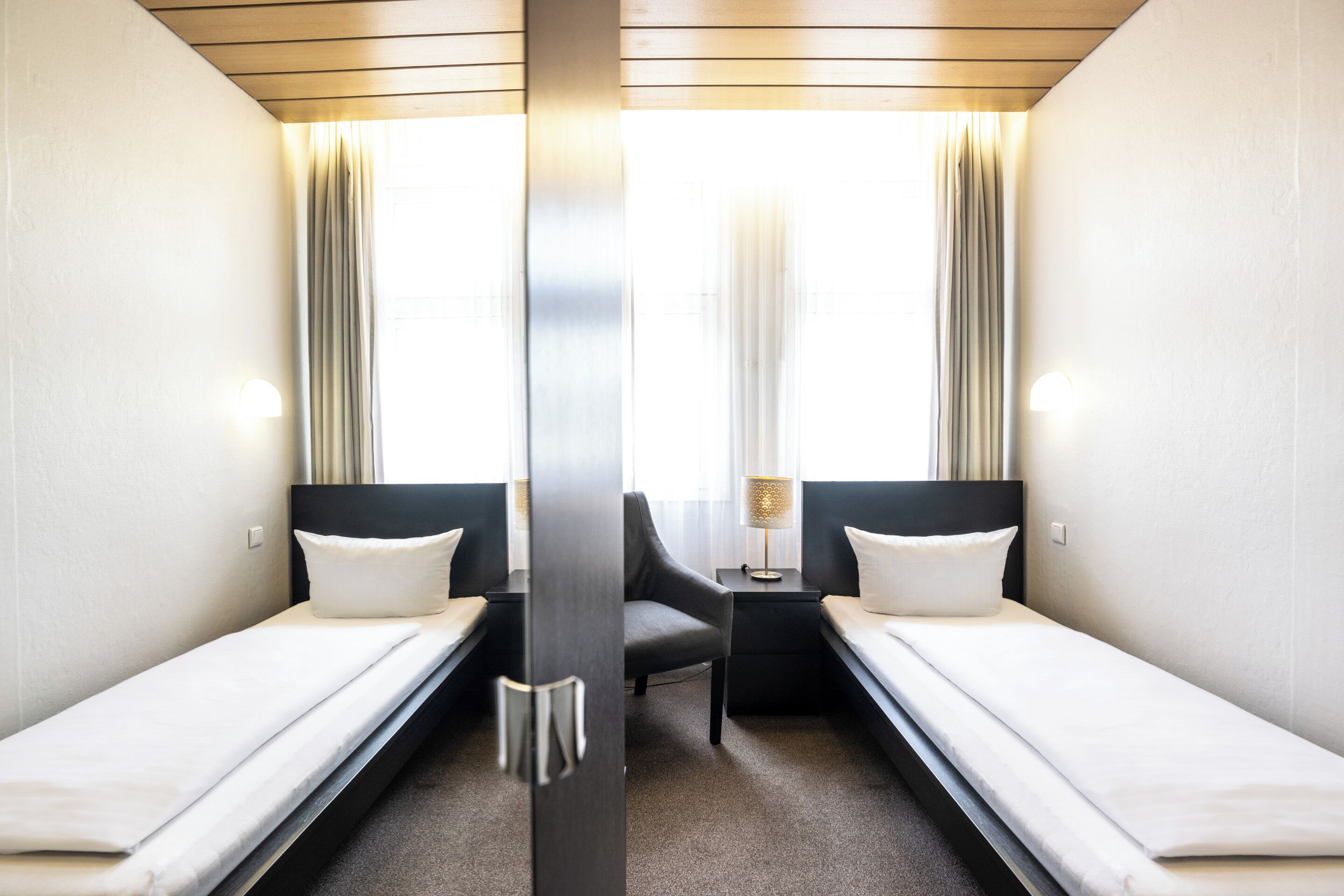 Ein Hotelzimmer mit zwei Einzelbetten, einem kleinen Tisch, einem Stuhl und einer Lampe.