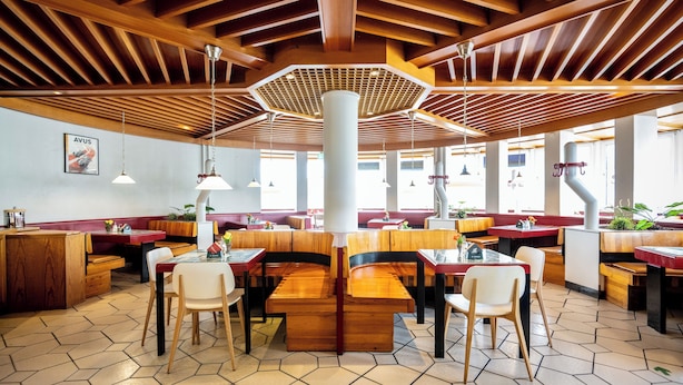 A restaurant with wooden ceiling beams, hexagonal ceiling light fixtures, and a central white pillar. - Raststättenhotel Avus (Berlin)
