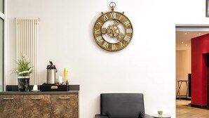 Un intérieur moderne avec un fauteuil en cuir noir, une horloge murale, un coin café et un radiateur.