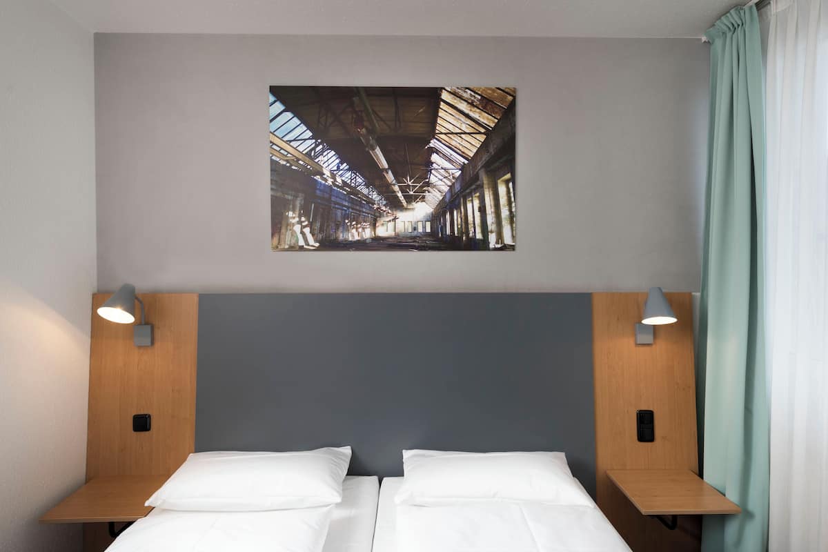 A hotel room with two beds, a wooden headboard, a wall-mounted artwork, and bedside lamps.