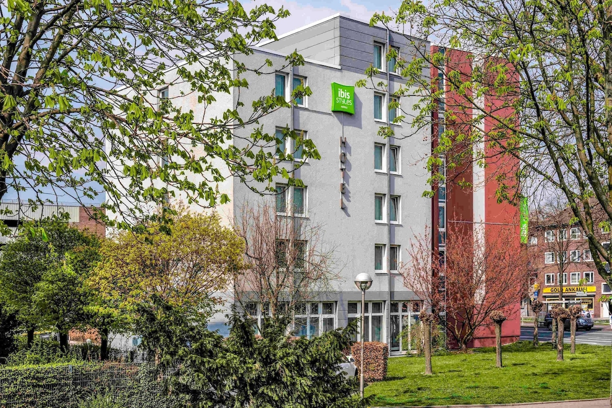 Ein Hotel mit modernem Design, ein Schild, das es als Teil der ibis Styles Hotelkette kennzeichnet, und ein sichtbarer Eingang.