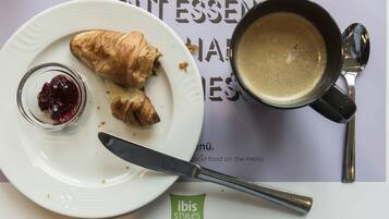 A plate with croissants and jam, a cup of coffee, and a spoon on a menu.