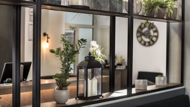 Un intérieur moderne avec un bureau en bois, une plante en pot, une lanterne noire et une horloge murale.