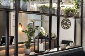 A modern interior with a wooden desk, a potted plant, a black lantern, and a wall clock. - ibis Styles Gelsenkirchen (Gelsenkirchen)
