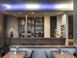 Un área de bar moderna con mostrador, estantes llenos de botellas y vasos, y asientos con mesas y sillas.