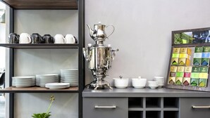 Une petite cuisine équipée d'un samovar en métal, de piles d'assiettes et d'une étagère où sont exposées des boîtes de thé.
