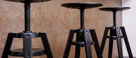 Three black metal stools with round tops and a central column, positioned against a textured wall.