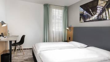 Ein Hotelzimmer mit Bett, Schreibtisch, Stuhl, Lampe und einem Bild an der Wand.