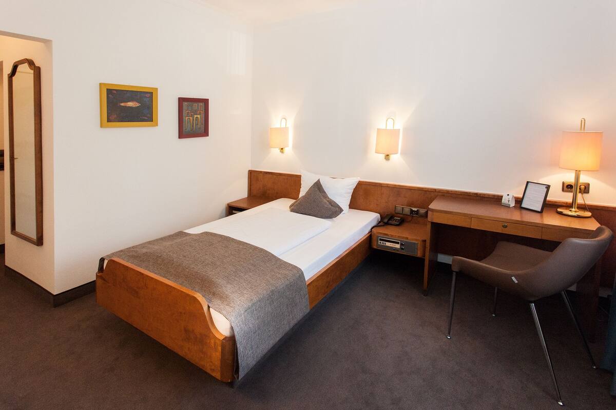 Een hotelkamer met een houten bed, een bureau, een stoel en twee wandlampen.