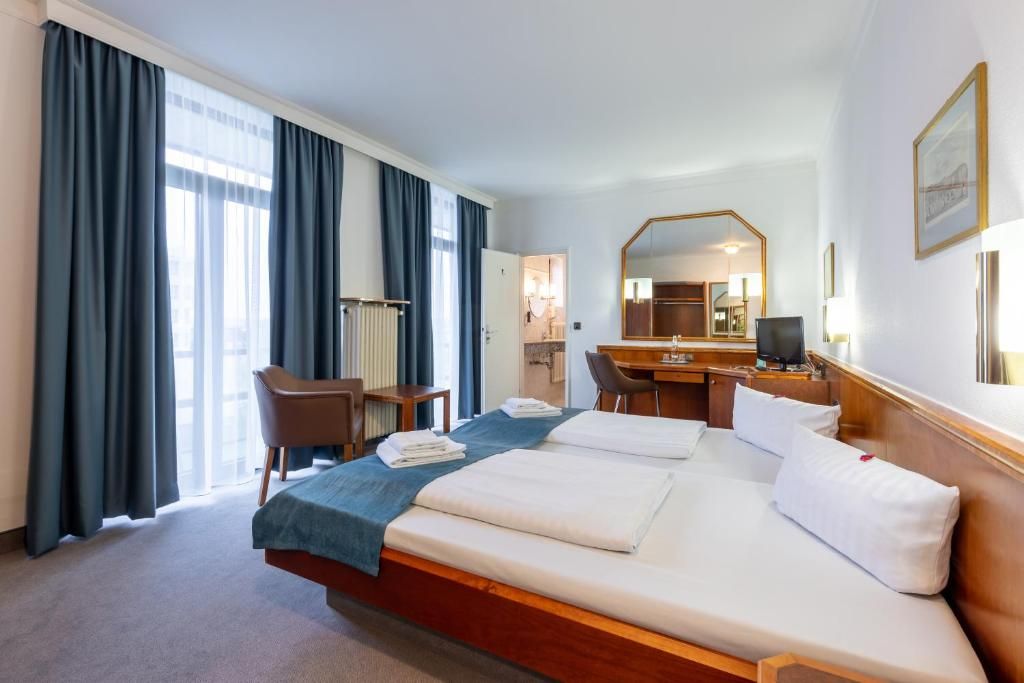 A hotel room with a large bed, a desk, a chair, and a mirror.