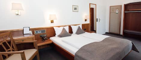Habitación de hotel con cama, escritorio, silla, mesita de noche y armario.