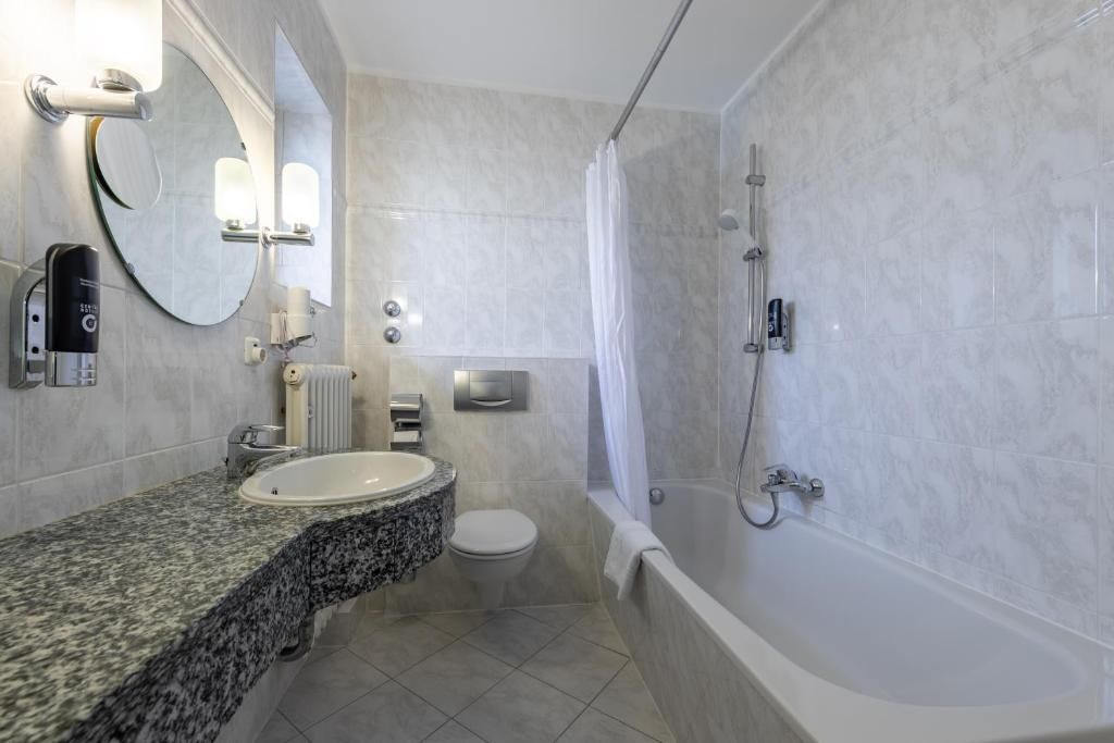 Une salle de bain moderne avec un lavabo sur un plan de travail en granit, des toilettes, une baignoire et une douche.