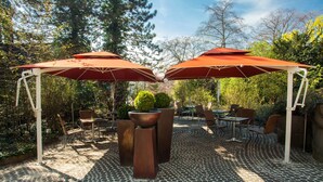 Une terrasse extérieure avec deux parasols rouges, une table ronde et plusieurs chaises.