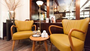 Un espace d’accueil avec deux fauteuils jaunes, une petite table ronde sur laquelle se trouve un plateau, un vase avec des branches et une lampe.