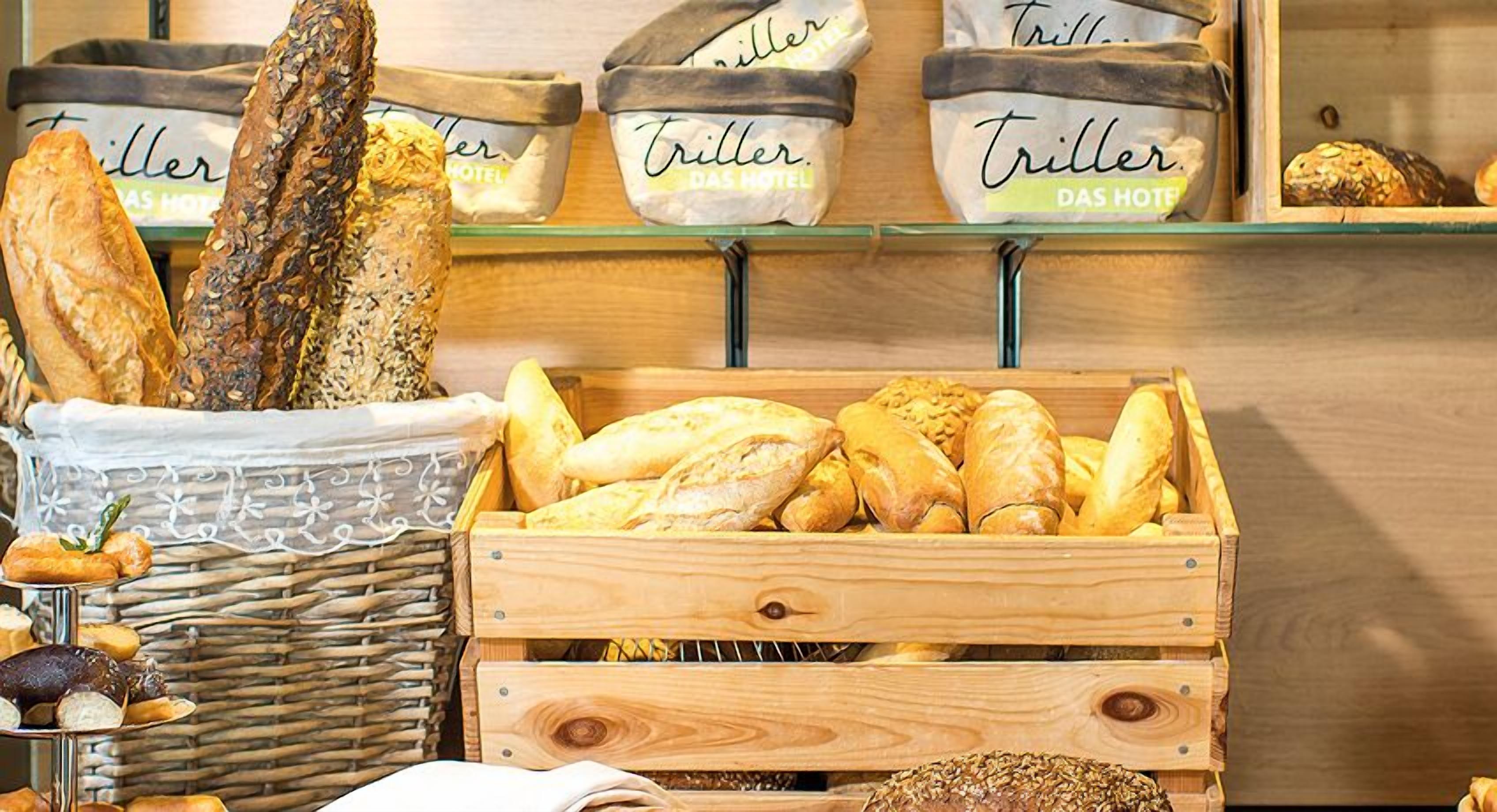 A bakery display with various types of bread, including baguettes and loaves, in wicker baskets and wooden crates.
