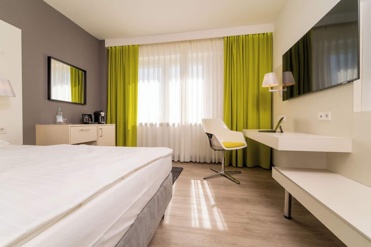A modern hotel room with a large bed, a desk, a chair, and a TV.